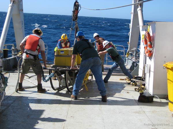 Crew steadying the sonar towfish to be lifted off the deck.